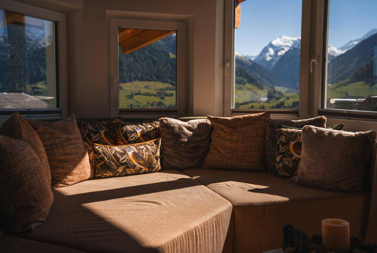 Gemütliche Sitzecke mit vielen Kissen und weitem Bergblick durch die Fenster.