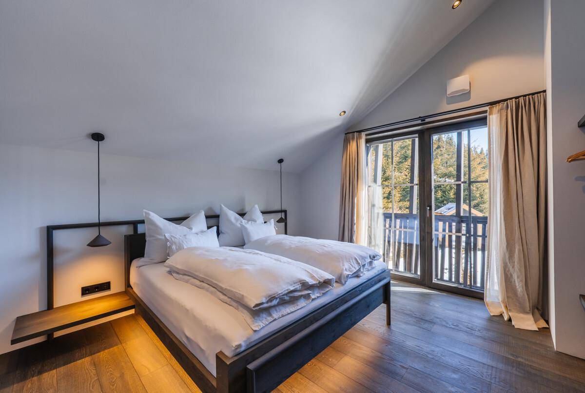 Schlafzimmer mit Doppelbett, Holzboden und Balkonzugang mit Blick auf die Berge.