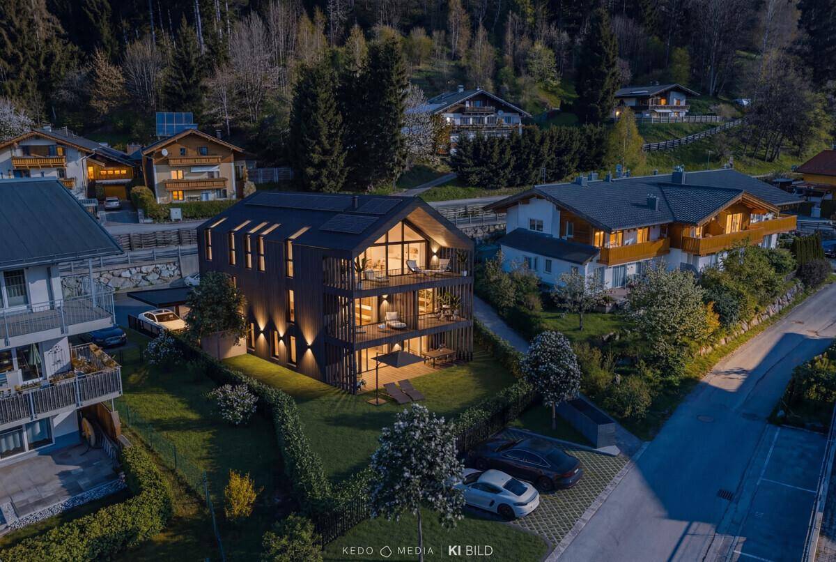 Beleuchtetes modernes Mehrfamilienhaus bei Nacht, umgeben von Natur und anderen Wohnhäusern in den Bergen.