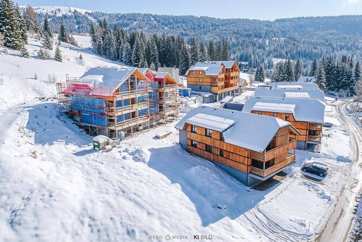 Luftaufnahme der im Bau befindlichen Holzgebäude in einer tief verschneiten Berglandschaft.