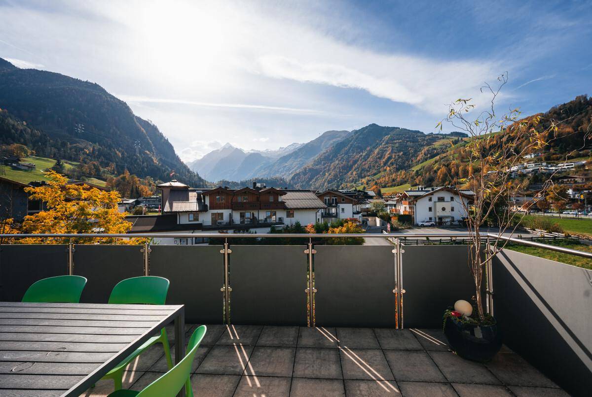 Sonnige Terrasse mit Esstisch und Stühlen, umgeben von einer beeindruckenden Berglandschaft.