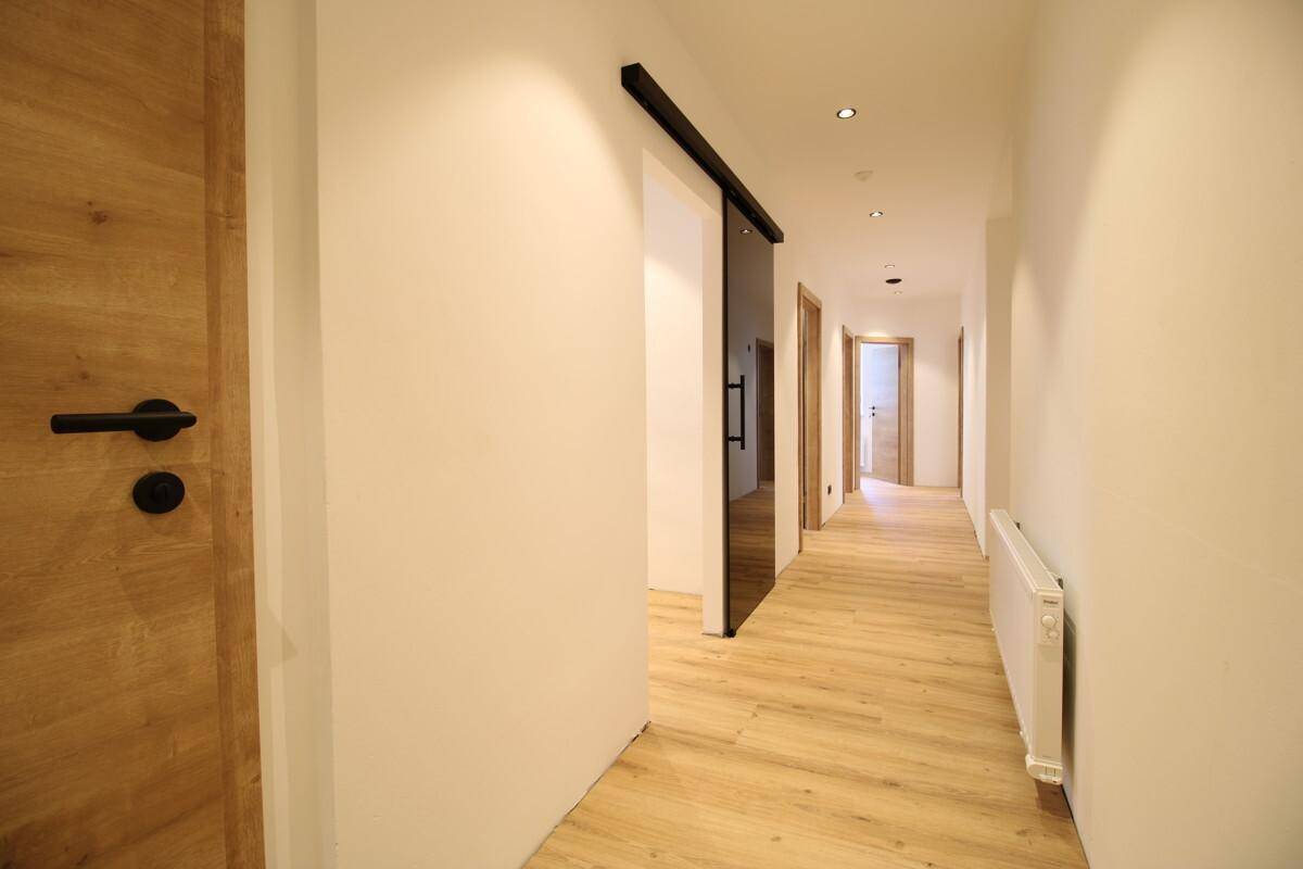 Heller Flur mit Holzboden, weißen Wänden und modernen Schiebetüren aus Glas.