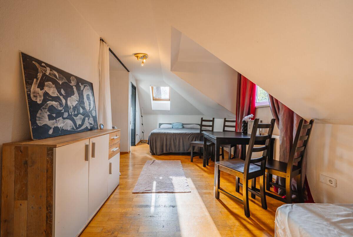 Dachgeschoss-Schlafzimmer mit Holzboden, Dachschrägen und einem Esstisch.