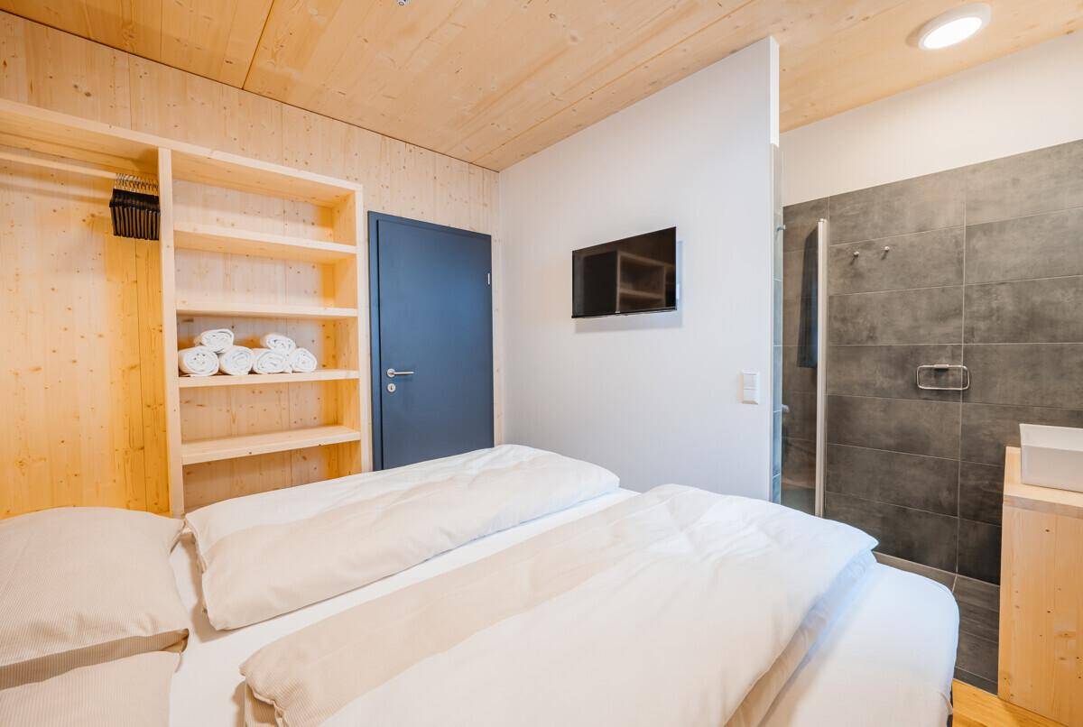 Schlafzimmer mit Doppelbett, offenem Kleiderschrank und integriertem Duschbereich für Komfort.