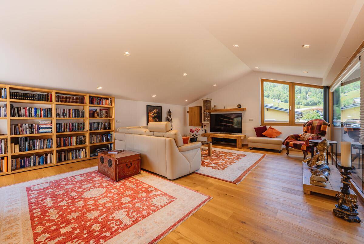 Großzügiges Wohnzimmer im Dachgeschoss mit Holzboden, Bücherregal und gemütlicher Sitzecke.
