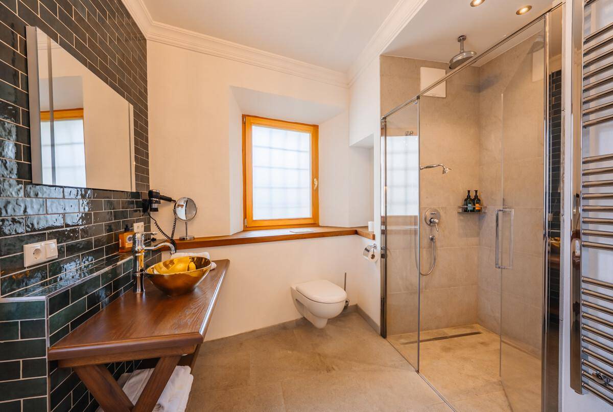 Modernes Badezimmer mit begehbarer Dusche, goldenem Waschbecken und Fenster.