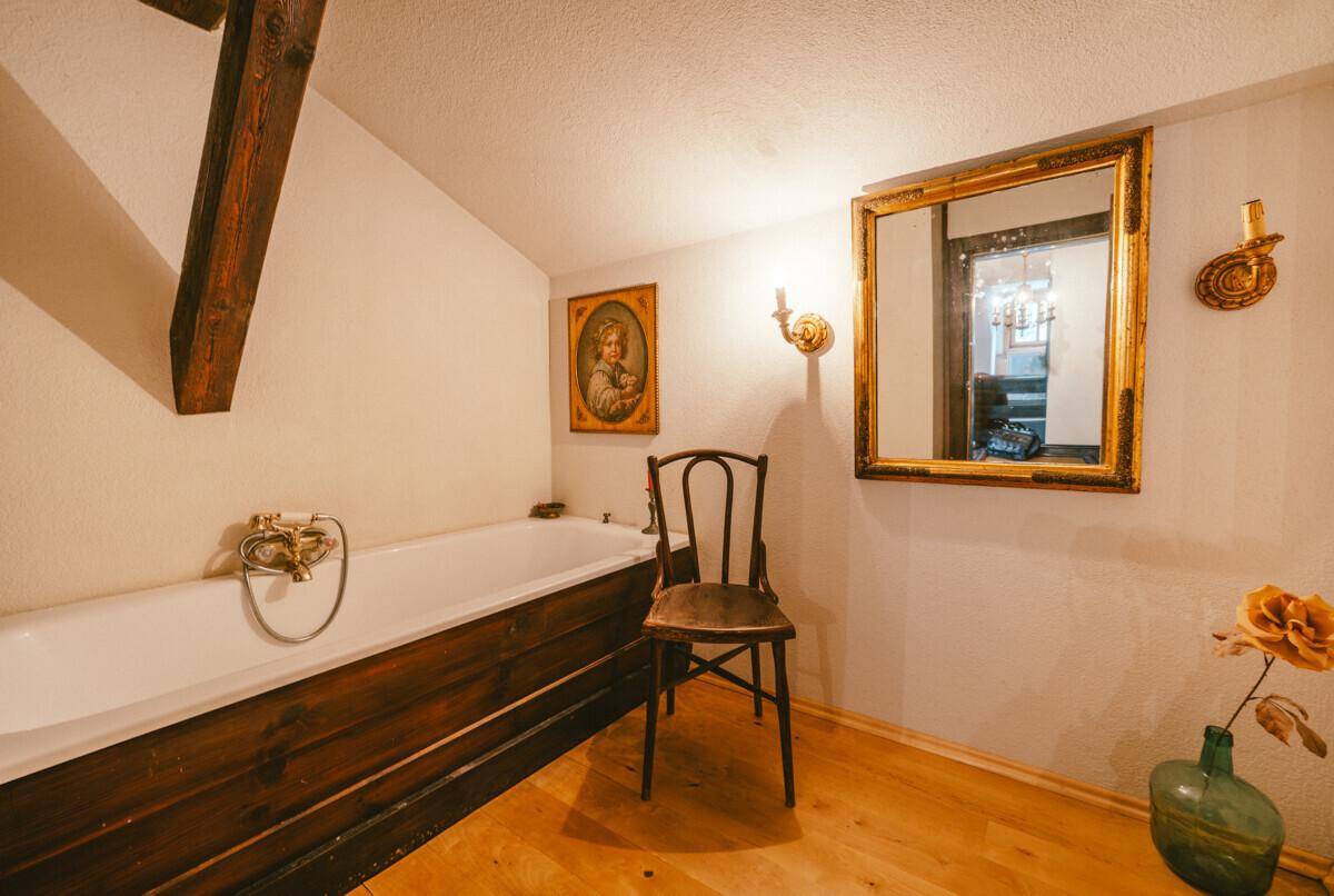 Badezimmer mit einer Badewanne, Holzbalken und einem großen, verzierten Spiegel.