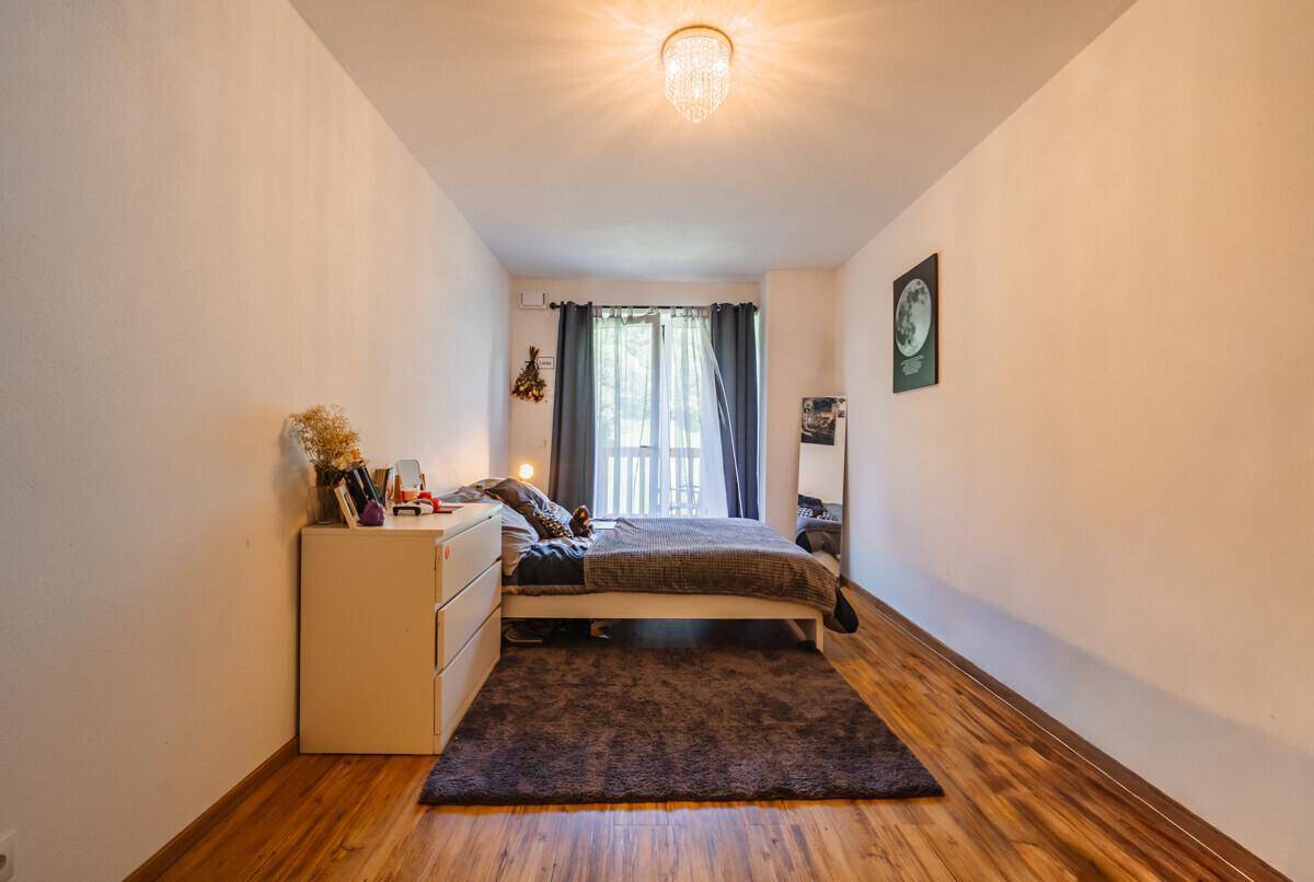 Gemütliches Schlafzimmer mit Holzboden, weißen Wänden und einem Fenster mit dunklen Vorhängen.