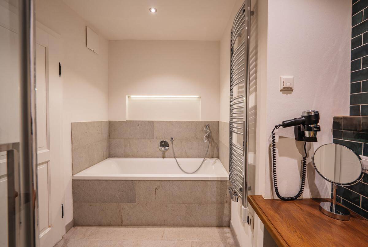 Badezimmer mit eingebauter Badewanne, beheiztem Handtuchhalter und Schminkspiegel.