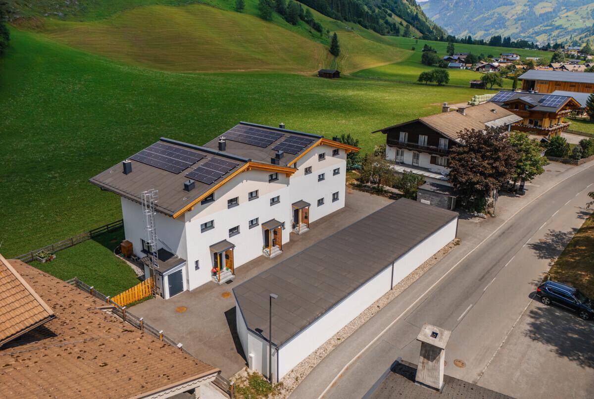 Rückansicht des Gebäudes mit Solarpaneelen auf dem Dach und einer langen Nebengebäude, umgeben von grüner Landschaft.