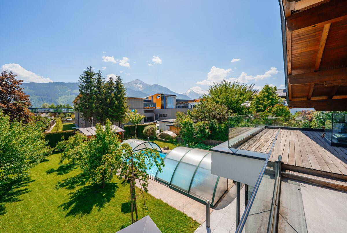 Gepflegter Garten mit Pool und Bergblick unter strahlend blauem Himmel.