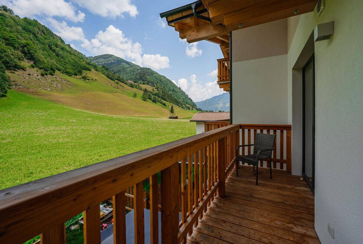 Geräumiger Balkon mit Holzgeländer, einem Stuhl und weitem Blick auf grüne Wiesen und Berge.