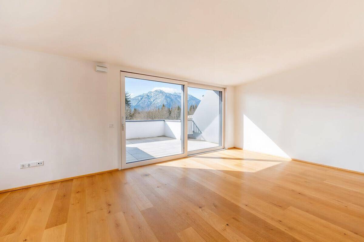 Heller Raum mit Holzboden, großen Fenstern und beeindruckendem Bergblick von der Terrasse.