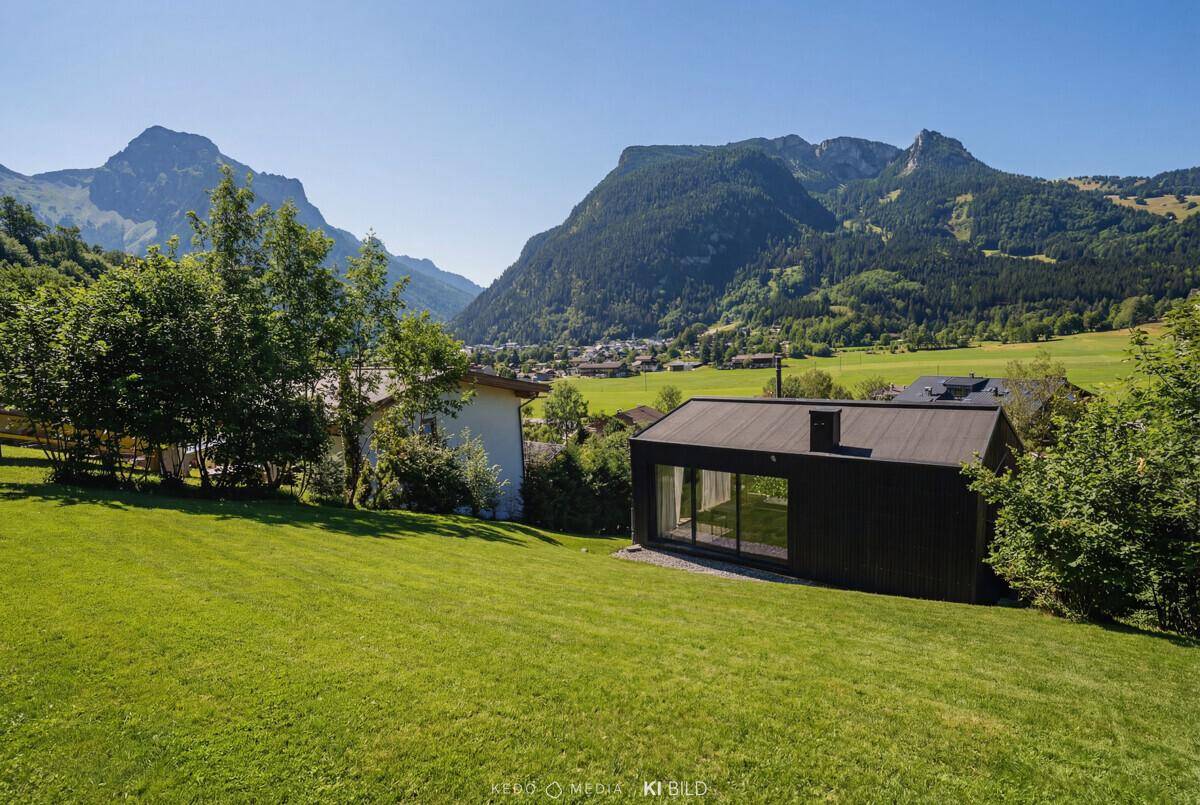 Modernes Haus mit Flachdach und Glasfronten in einer weiten grünen Landschaft mit Bergblick.