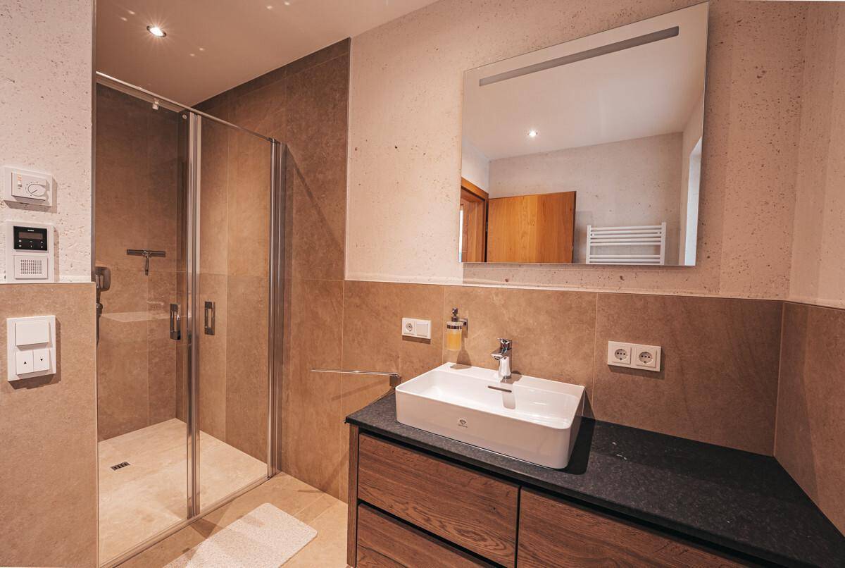 Modernes Badezimmer mit begehbarer Dusche, Einzelwaschbecken und dunklen Fliesen.
