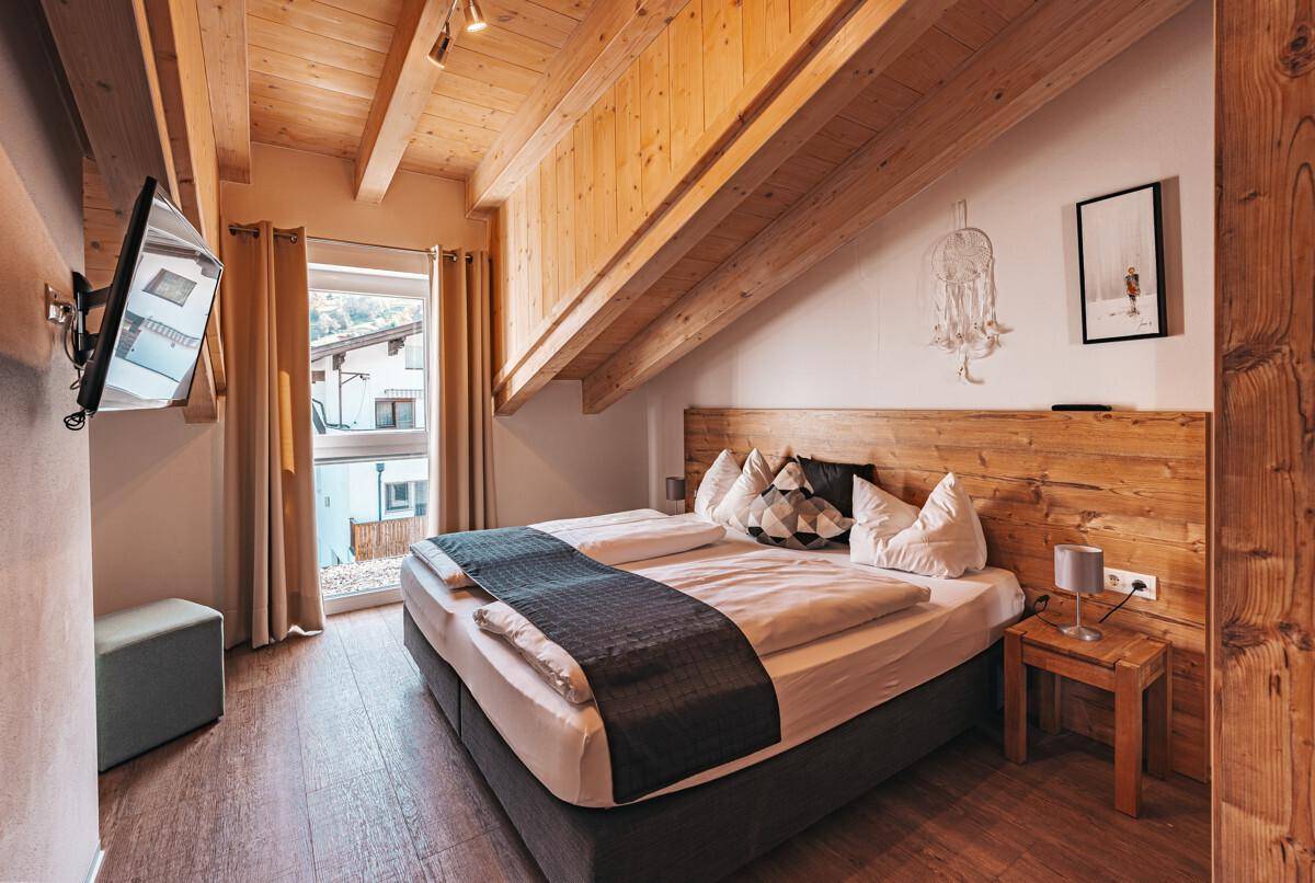 Gemütliches Schlafzimmer mit Doppelbett, Holzkopfteil und sichtbaren Holzbalken an der Dachschräge.