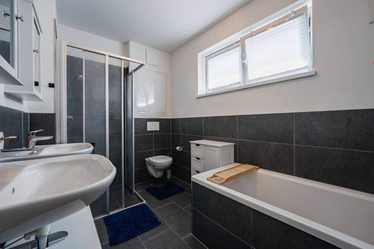 Modernes Badezimmer mit dunklen Fliesen, Doppelwaschbecken, Dusche und Badewanne.