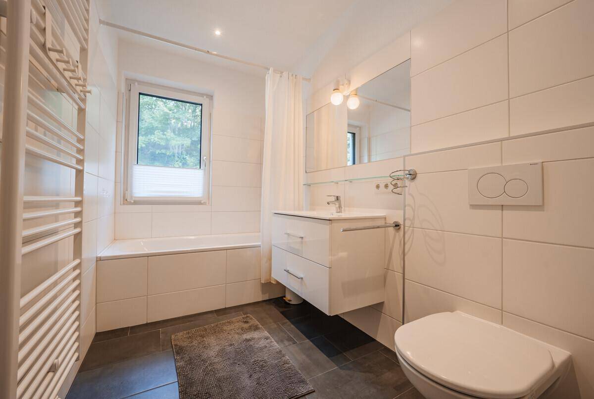 Helles Badezimmer mit Badewanne, Fenster und beheiztem Handtuchhalter.