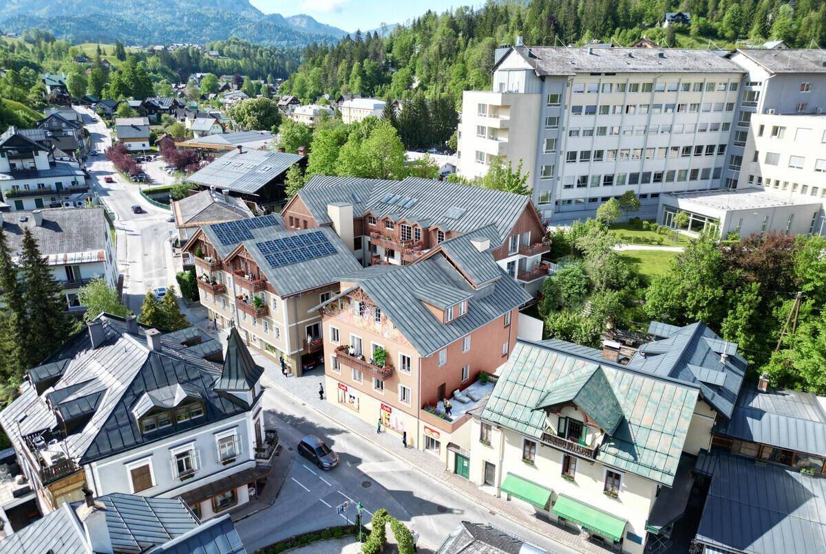 Luftaufnahme der Stadt mit dem Gebäudekomplex, umliegenden Häusern und grüner Landschaft.
