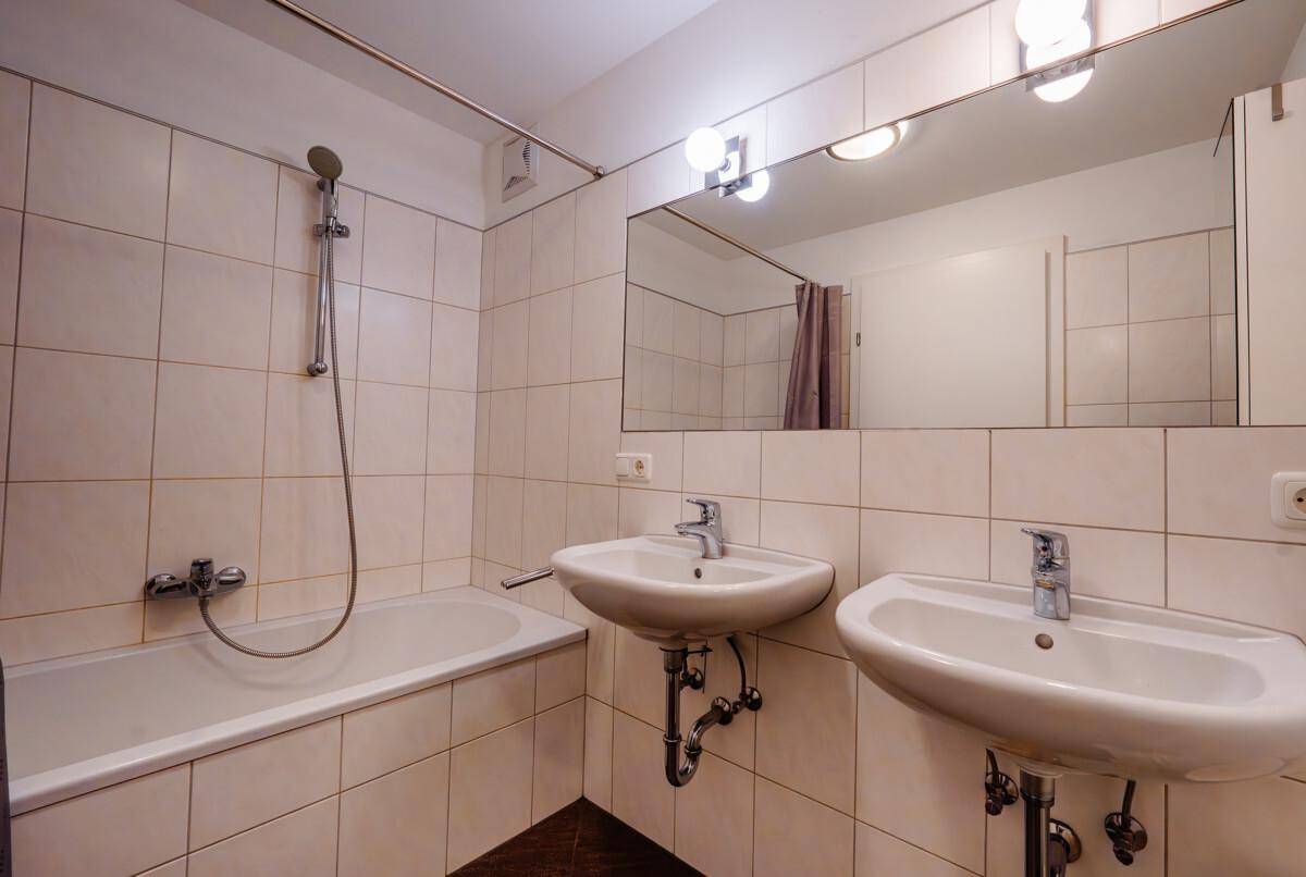 Funktionales Badezimmer mit zwei Waschbecken, Badewanne und weißen Fliesen an den Wänden.