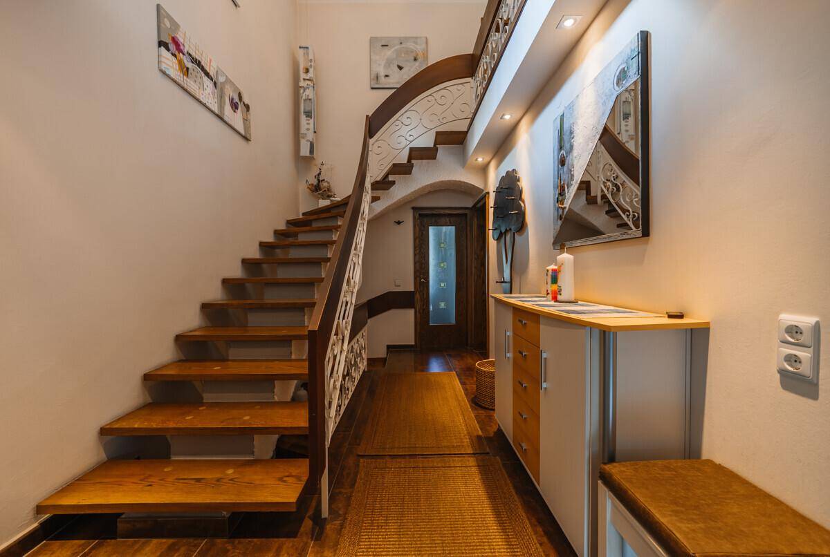 Geräumiger Flur mit Holztreppe, schmiedeeisernem Geländer und moderner Beleuchtung.
