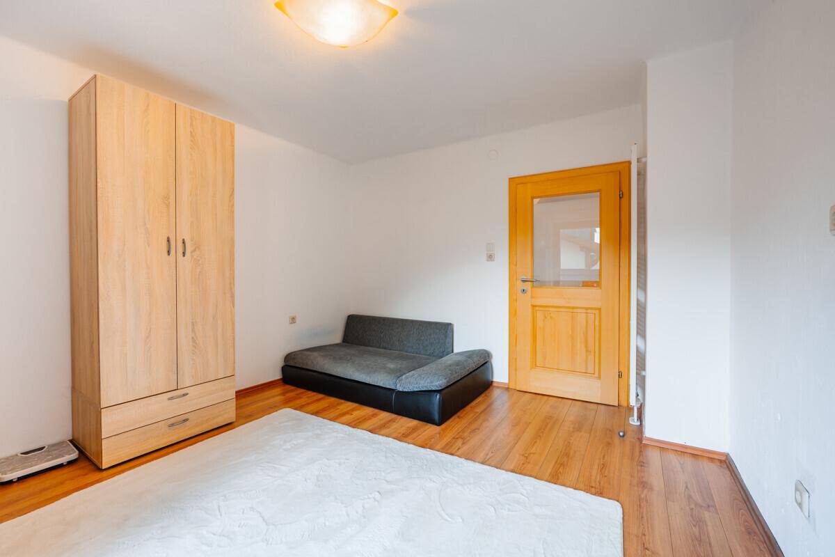 Schlafzimmer mit Holzboden, Kleiderschrank und einem kleinen Sofa, hell und funktional.