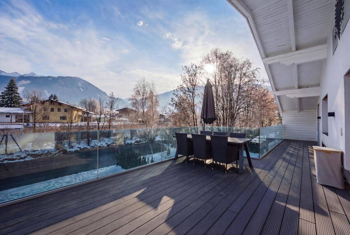 Großer Balkon mit Holzboden, Sitzgelegenheiten und Panoramablick auf die verschneiten Berge.