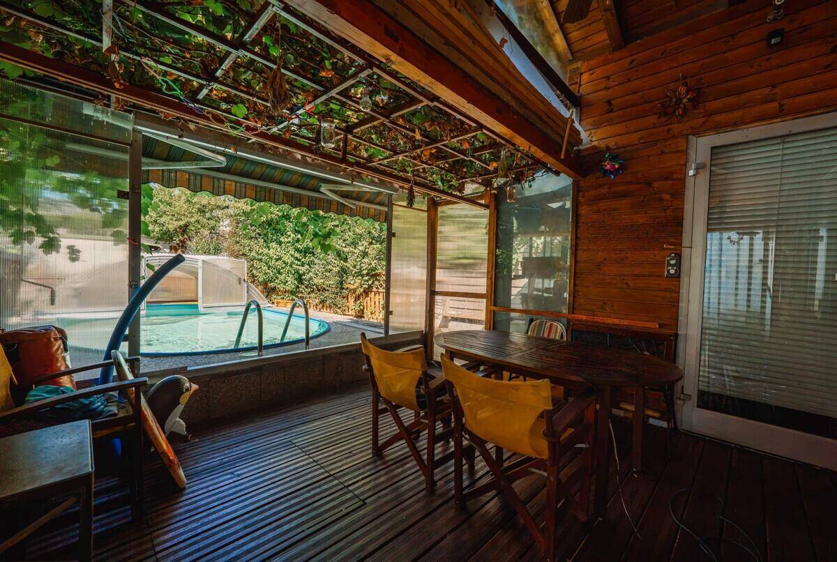 Überdachter Sitzbereich mit Holzwänden und Blick auf den Pool im sonnigen Garten.