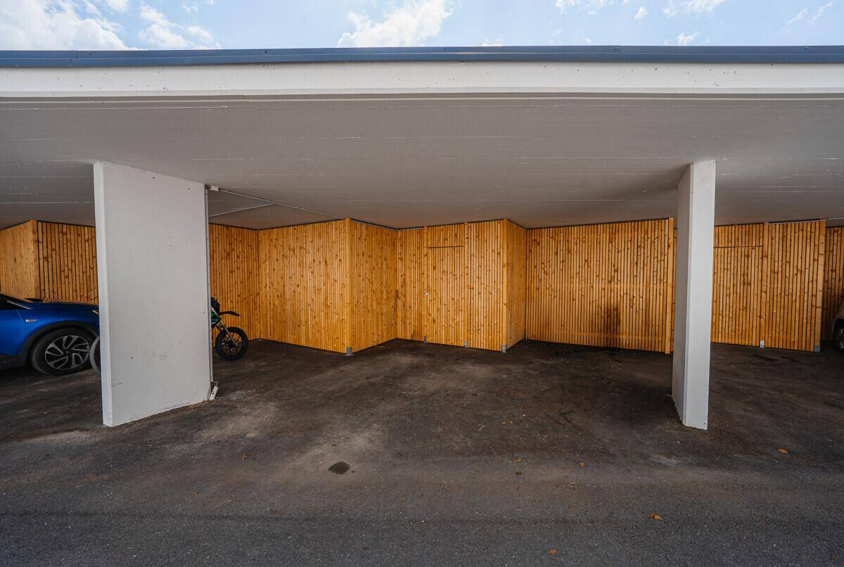 Überdachter Parkbereich mit Holzabtrennungen für einzelne Stellplätze und sichtbaren Fahrzeugen.