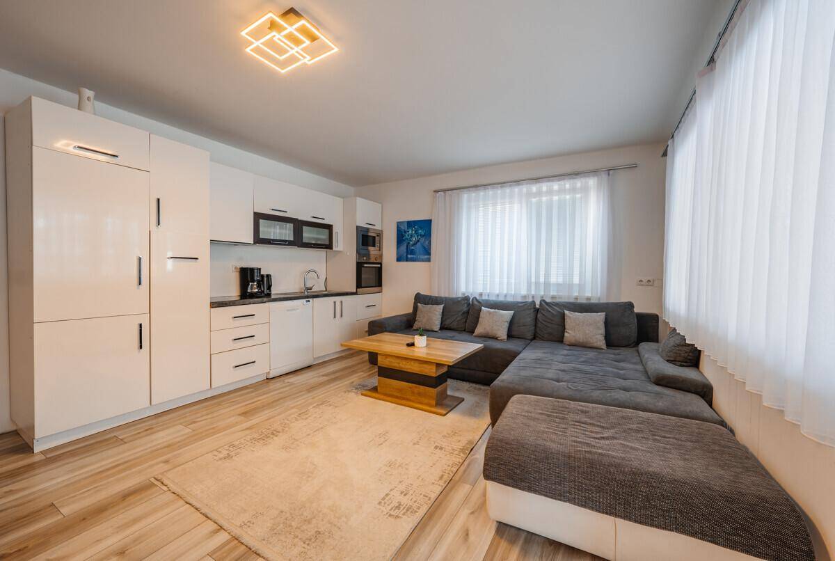 Wohnbereich mit integrierter Küchenzeile, großem Sofa und hellem Holzfußboden.