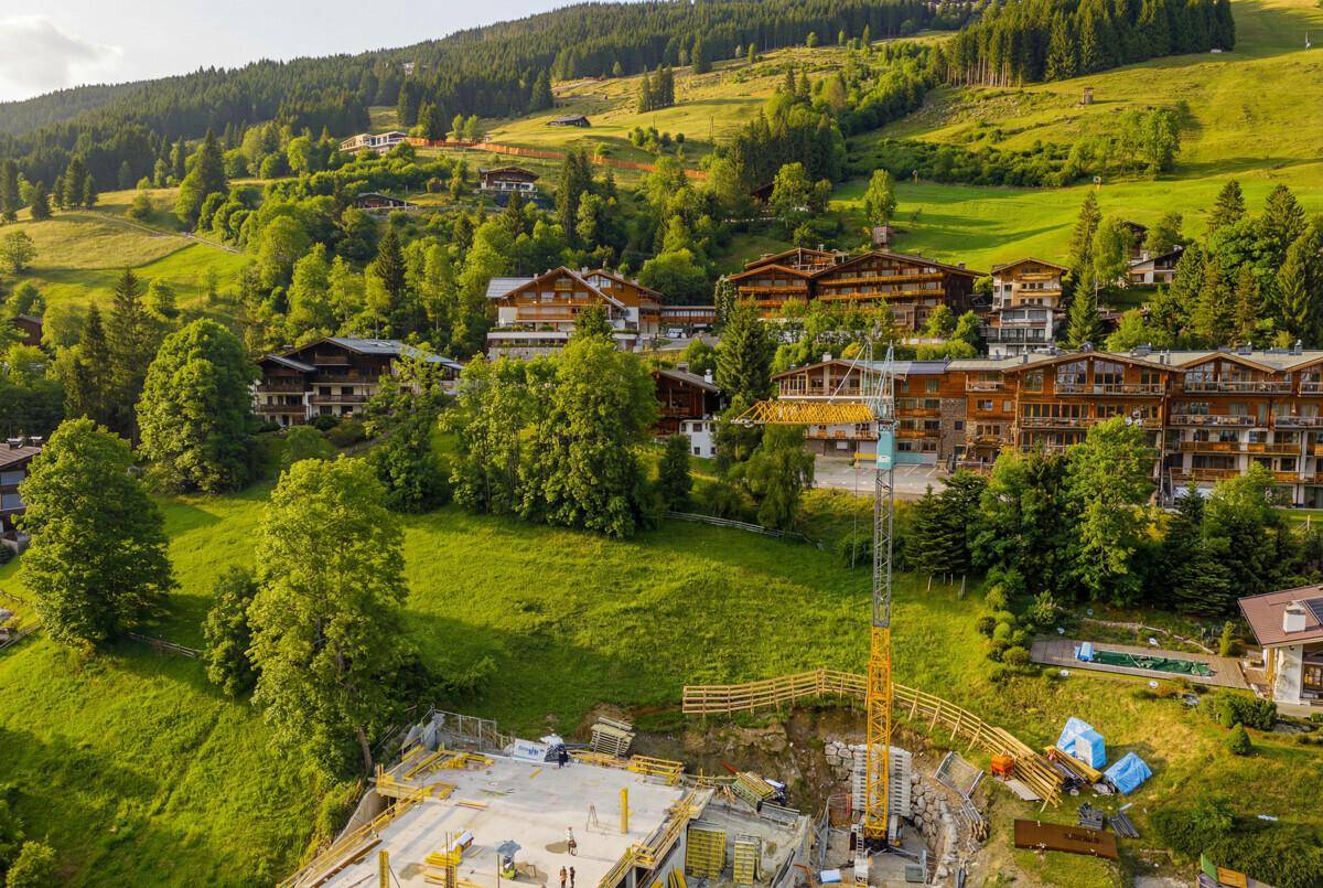 Panoramablick auf eine Baustelle in einem malerischen alpinen Dorf mit bewaldeten Hängen und traditionellen Häusern.