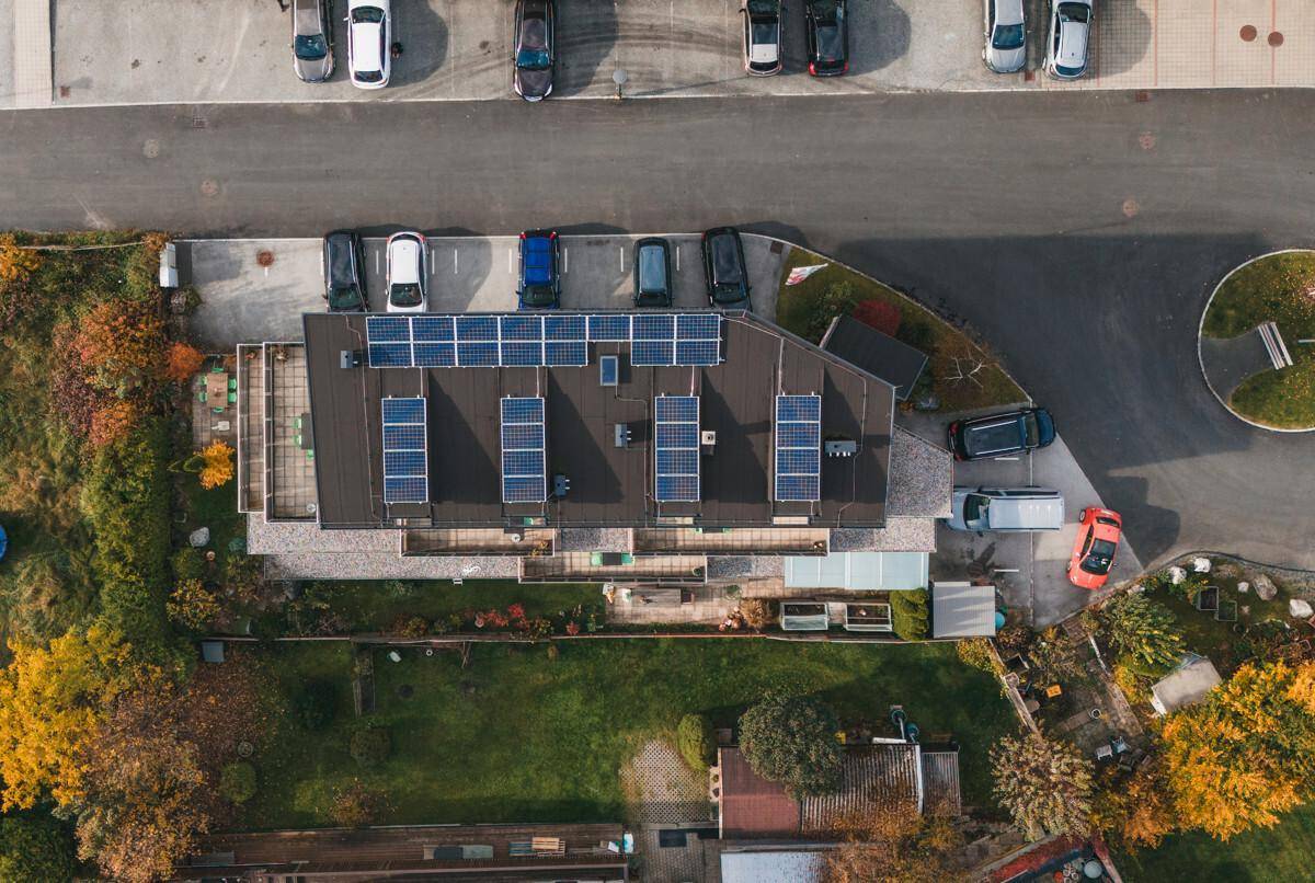Luftaufnahme eines Gebäudes mit Photovoltaikanlage auf dem Dach und umliegenden Parkplätzen.
