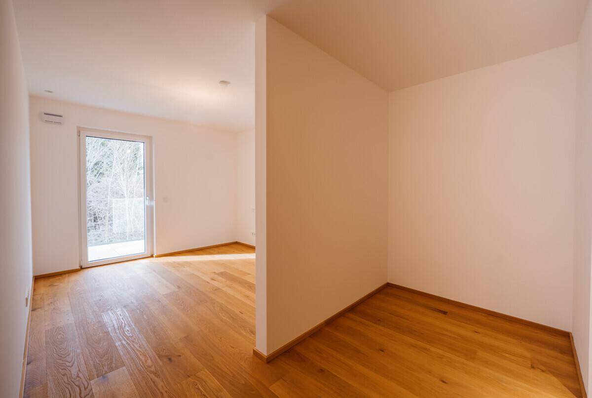 Leerer Raum mit Holzboden und Zugang zu einem Balkon oder einer kleinen Terrasse.