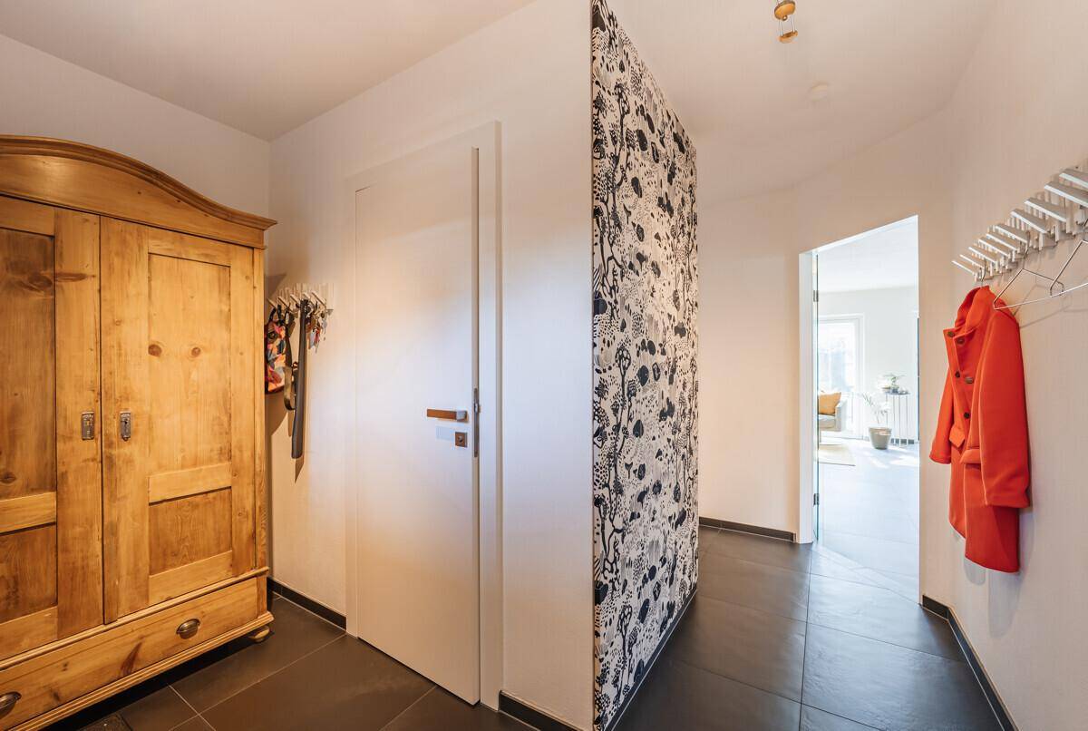 Heller Flur mit Holzkleiderschrank, dunklen Fliesen und dekorativer Tapete.