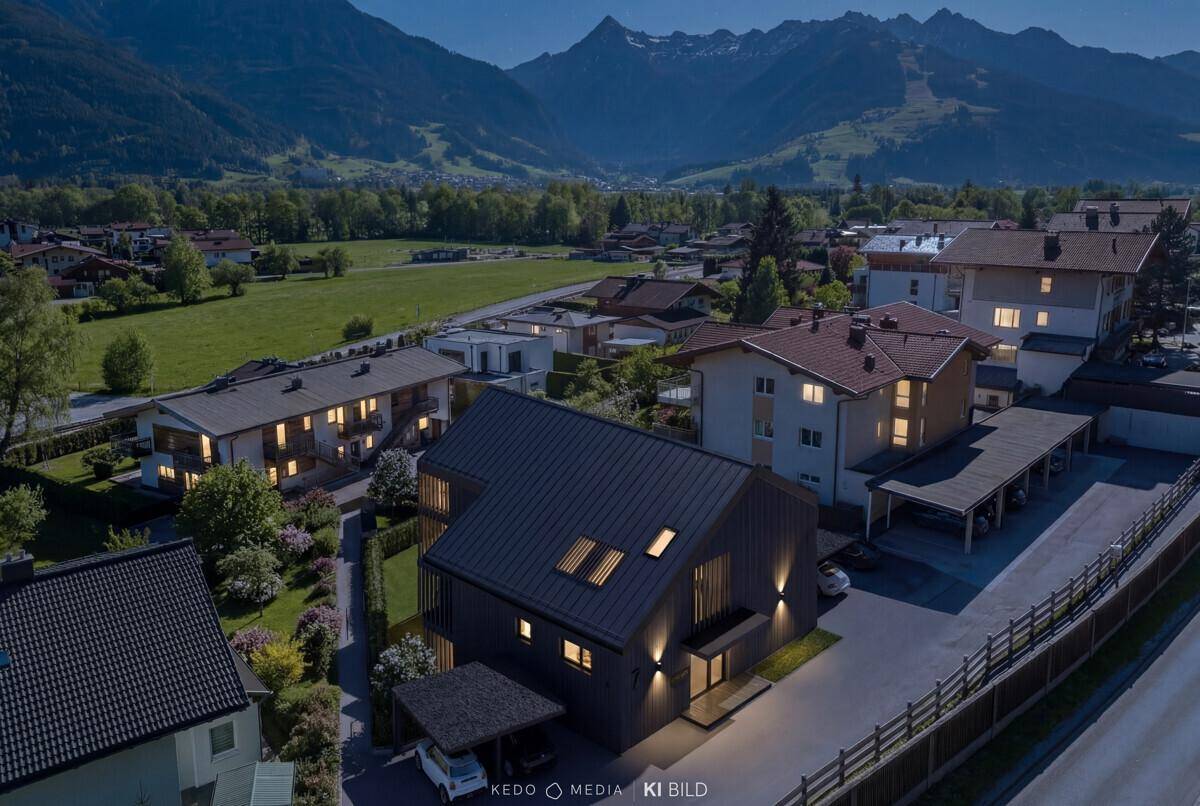 Moderne Wohnanlage in alpiner Landschaft mit Bergblick bei Dämmerung und beleuchteten Häusern.