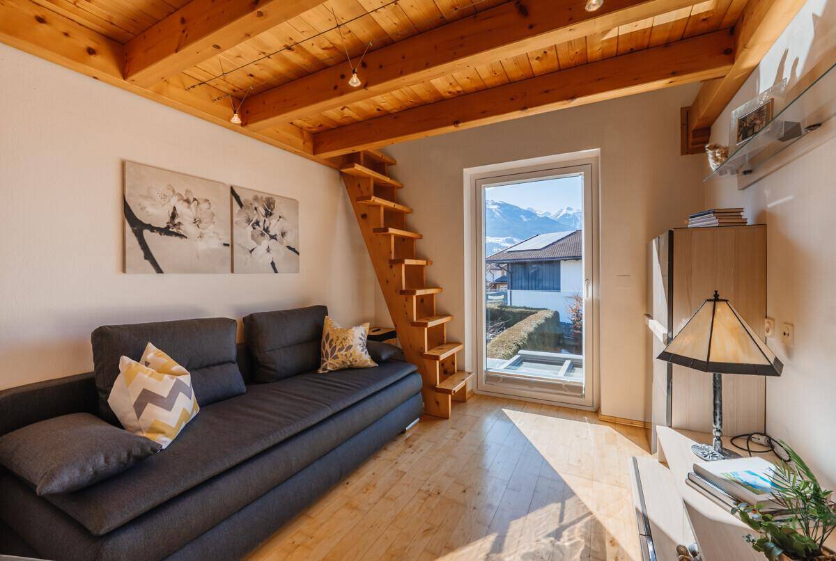 Gemütlicher Raum mit Holzbalkendecke, Sofa und Treppe zu einer oberen Ebene mit Bergblick.