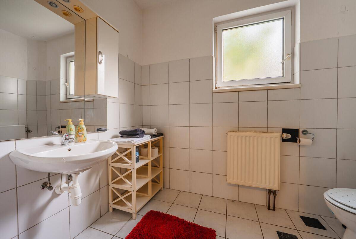 Einfaches Badezimmer mit Waschbecken, WC, Fliesenboden und einem Fenster für Tageslicht.