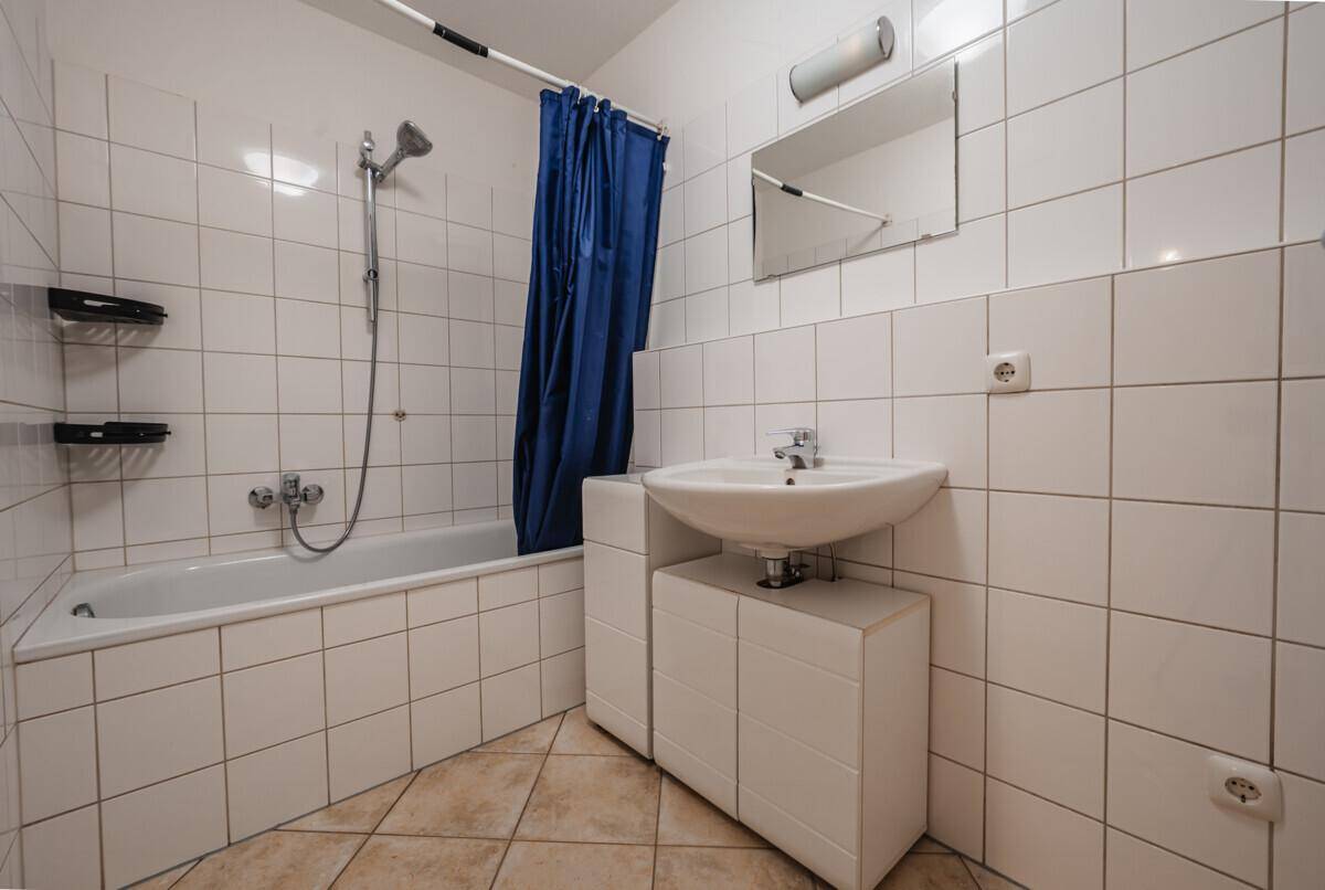 Badezimmer mit weißen Fliesen, Badewanne mit Duschfunktion und Waschbecken.