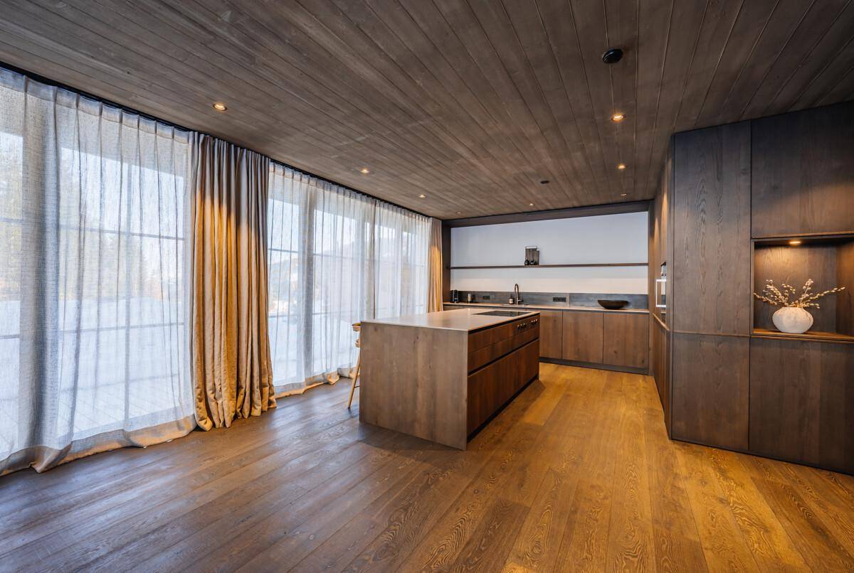 Moderne Holzküche mit Kochinsel, integrierten Geräten und großen Fenstern.