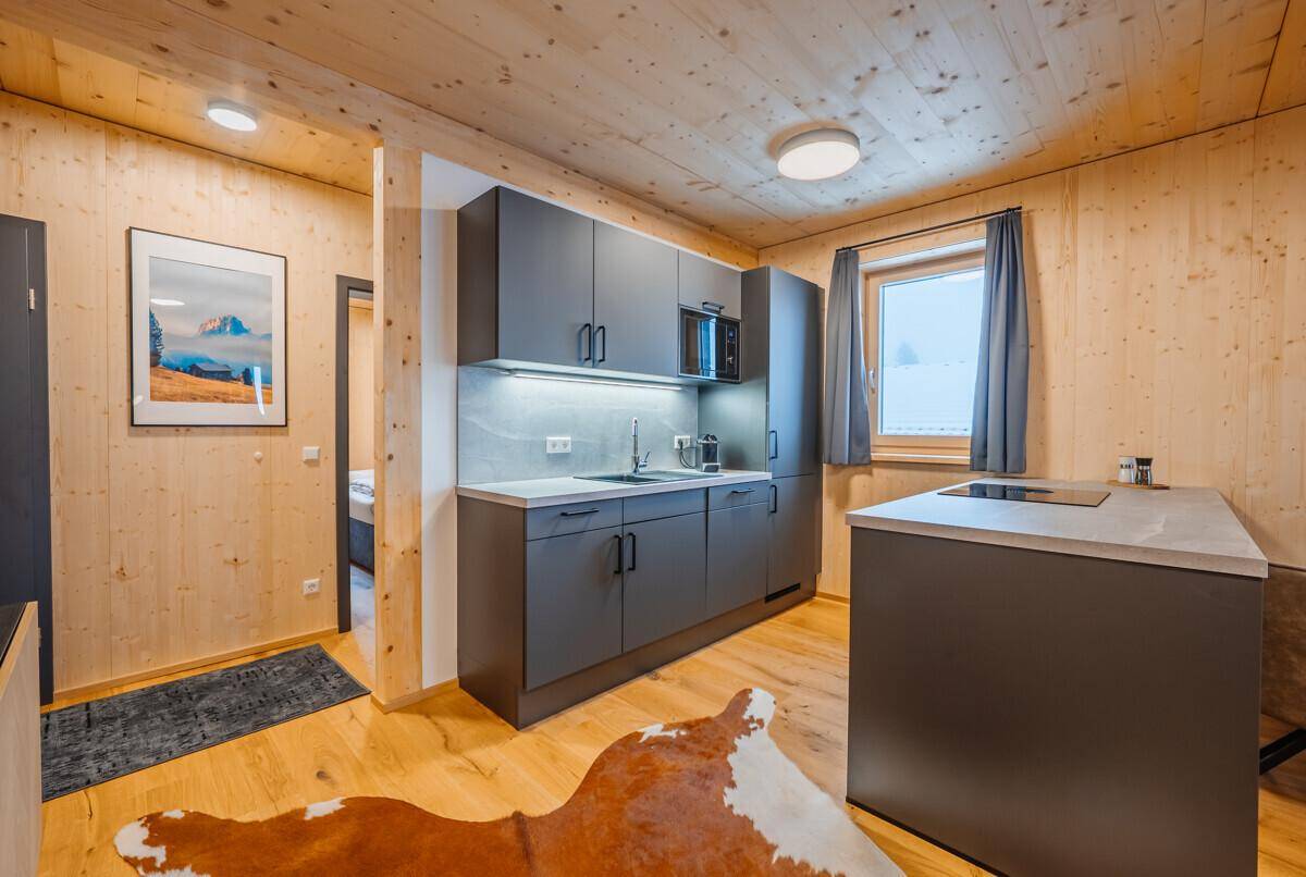 Moderne Einbauküche mit dunklen Schränken und Holzvertäfelung, integriert in einen offenen Wohnbereich.