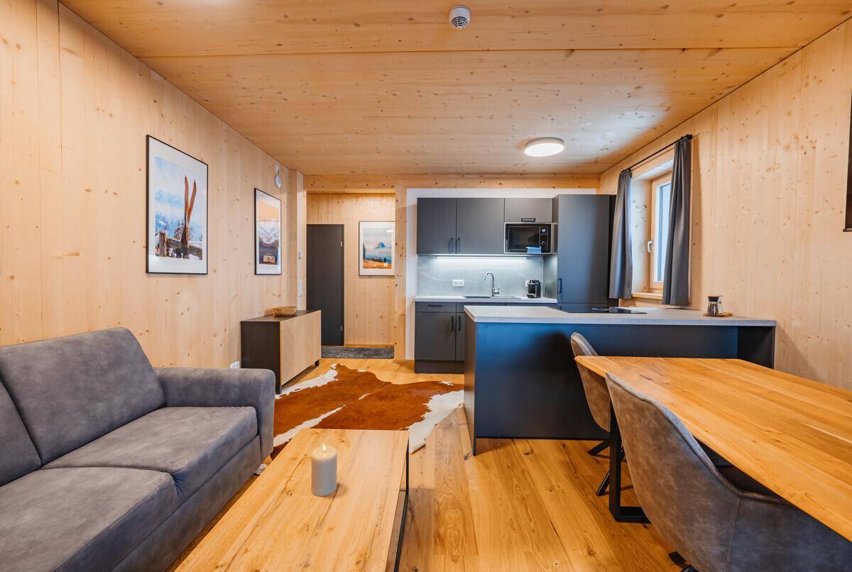 Heller Wohn-Essbereich mit integrierter Küche, Holzböden und gemütlicher Einrichtung im alpinen Stil.