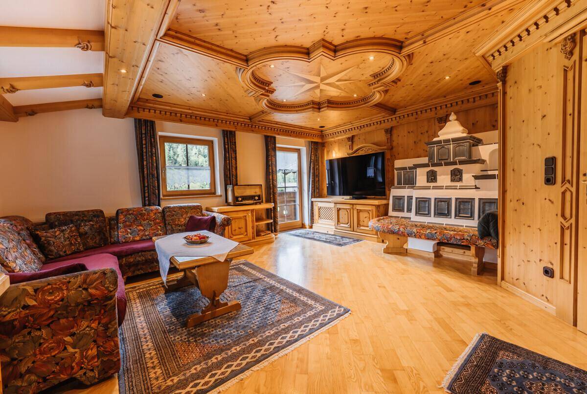 Gemütliches Wohnzimmer im alpinen Stil mit Holzboden, Kachelofen und traditionellen Möbeln.