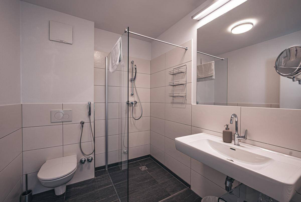 Helles Badezimmer mit ebenerdiger Dusche, wandhängendem WC und modernem Waschbecken.