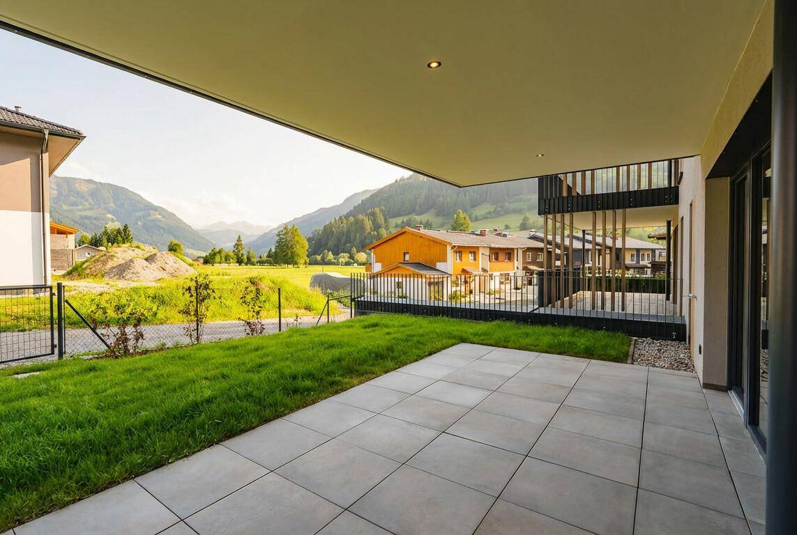 Große, überdachte Terrasse mit Fliesenboden und Rasenfläche, umgeben von grünen Bergen.