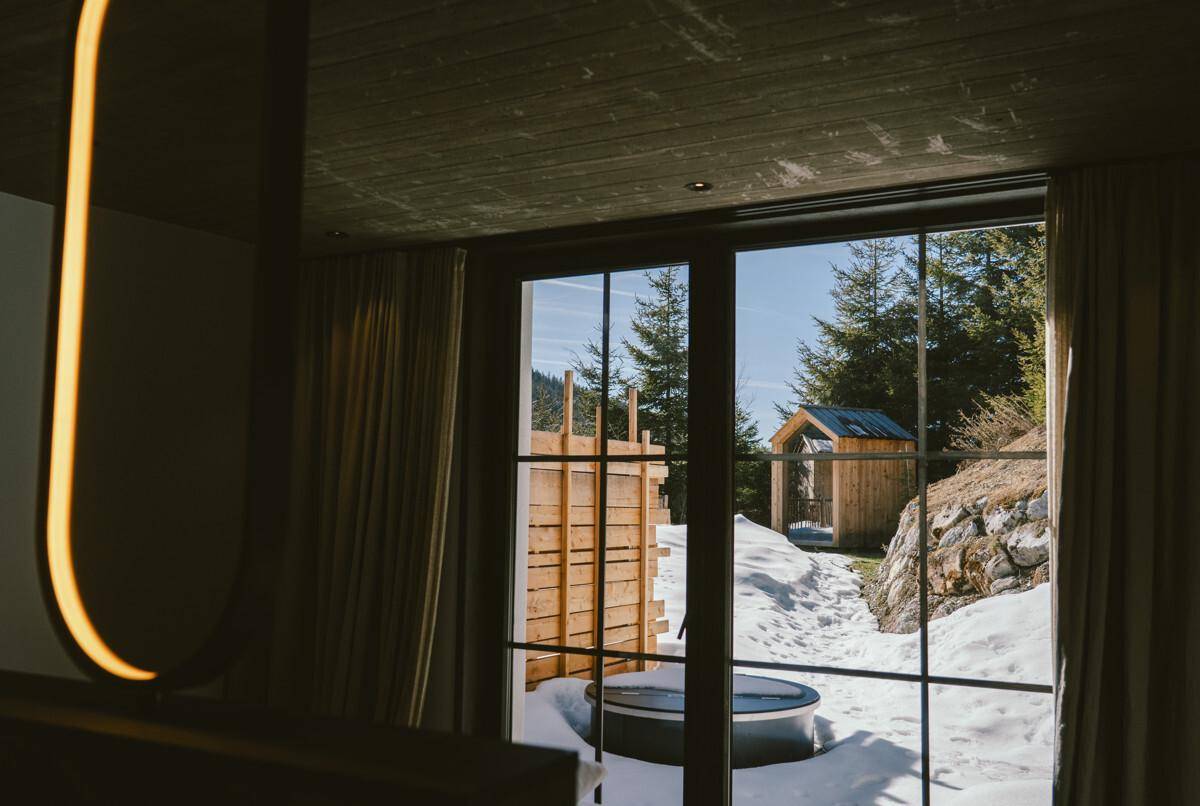 Blick aus dem Schlafzimmerfenster auf die verschneite Berglandschaft mit einem Hot Tub.