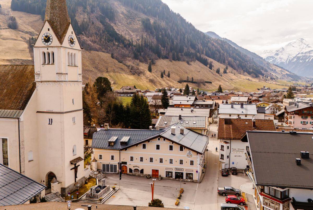 Panoramablick auf ein alpines Dorf mit Kirche, Bergen und traditionellen Gebäuden.
