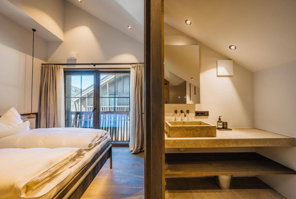 Schlafzimmer mit integriertem Waschbereich, modernem Steinwaschbecken und großem Spiegel.