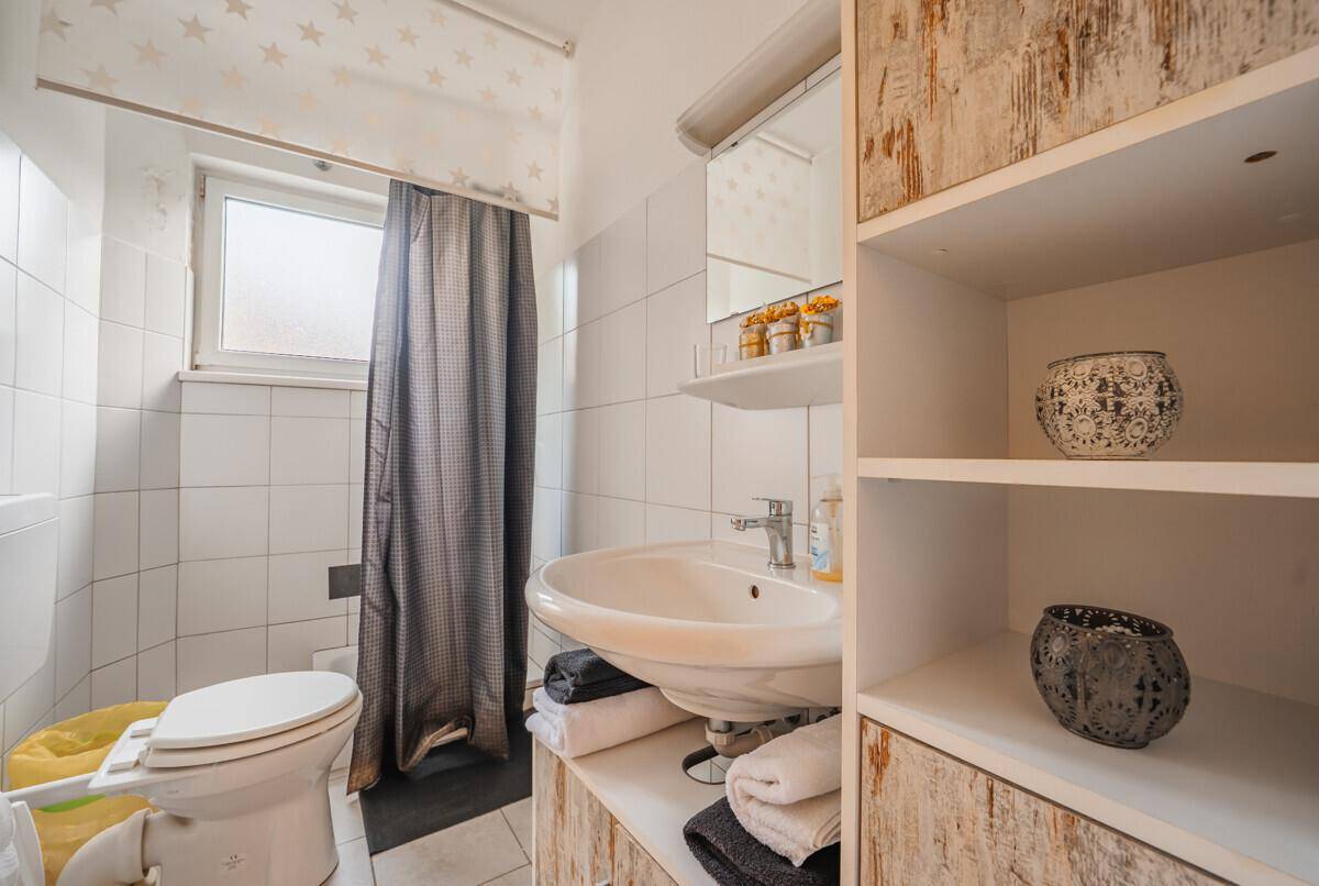 Badezimmer mit Waschbecken, WC, Fliesenboden und Fenster, schlicht und funktional eingerichtet.