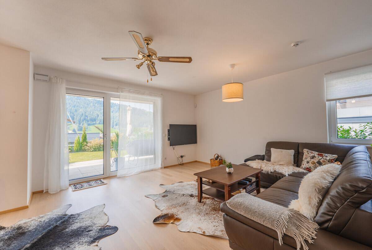 Gemütliches Wohnzimmer mit Ledersofa, Deckenventilator und Zugang zur Terrasse.