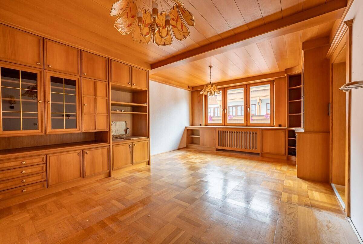 Wohnzimmer mit Holzbalkendecke, Parkettboden und großen Fenstern, ausgestattet mit Einbauschränken.